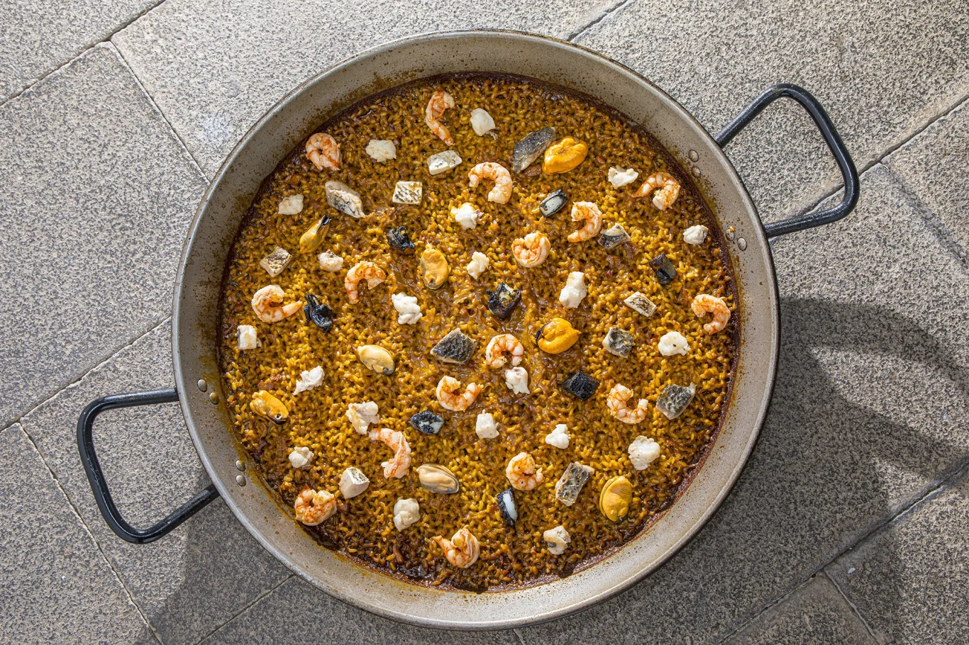 Paella mit Garnelen, Muscheln und Gemüse in einer großen Pfanne serviert.