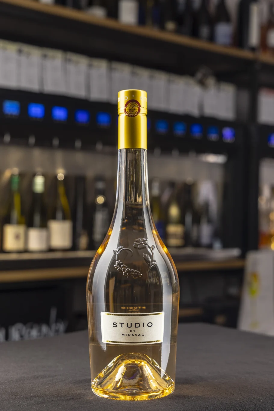 Eine Flasche Roséwein steht auf einem Tisch, im Hintergrund Weinflaschen im Regal.