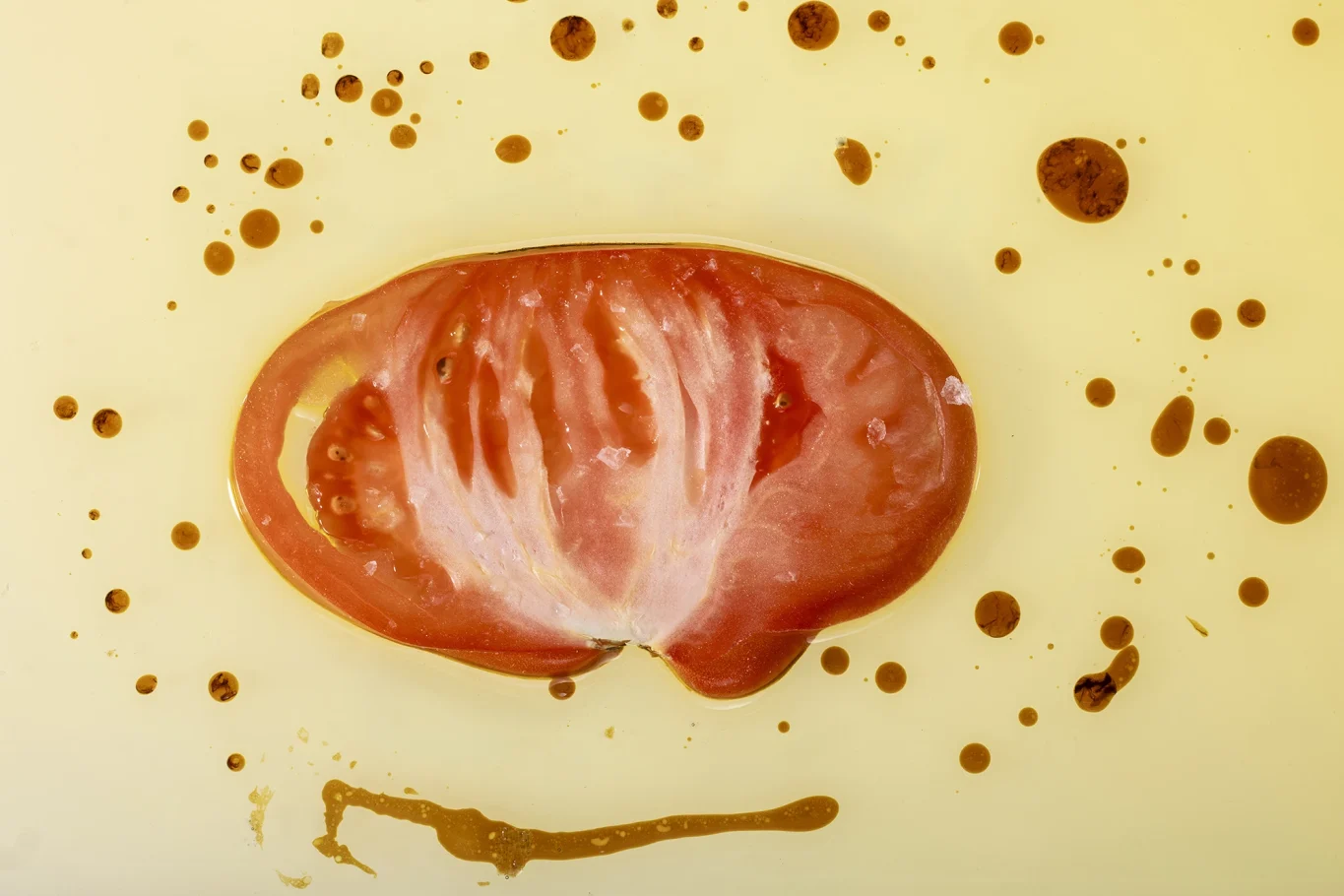 Eine Scheibe Tomate auf gelbem Hintergrund mit Spritzern von brauner Soße.