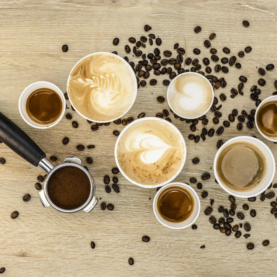 Verschiedene Kaffeetassen mit Kaffeebohnen und einem Kaffeeverteiler auf Holzuntergrund.