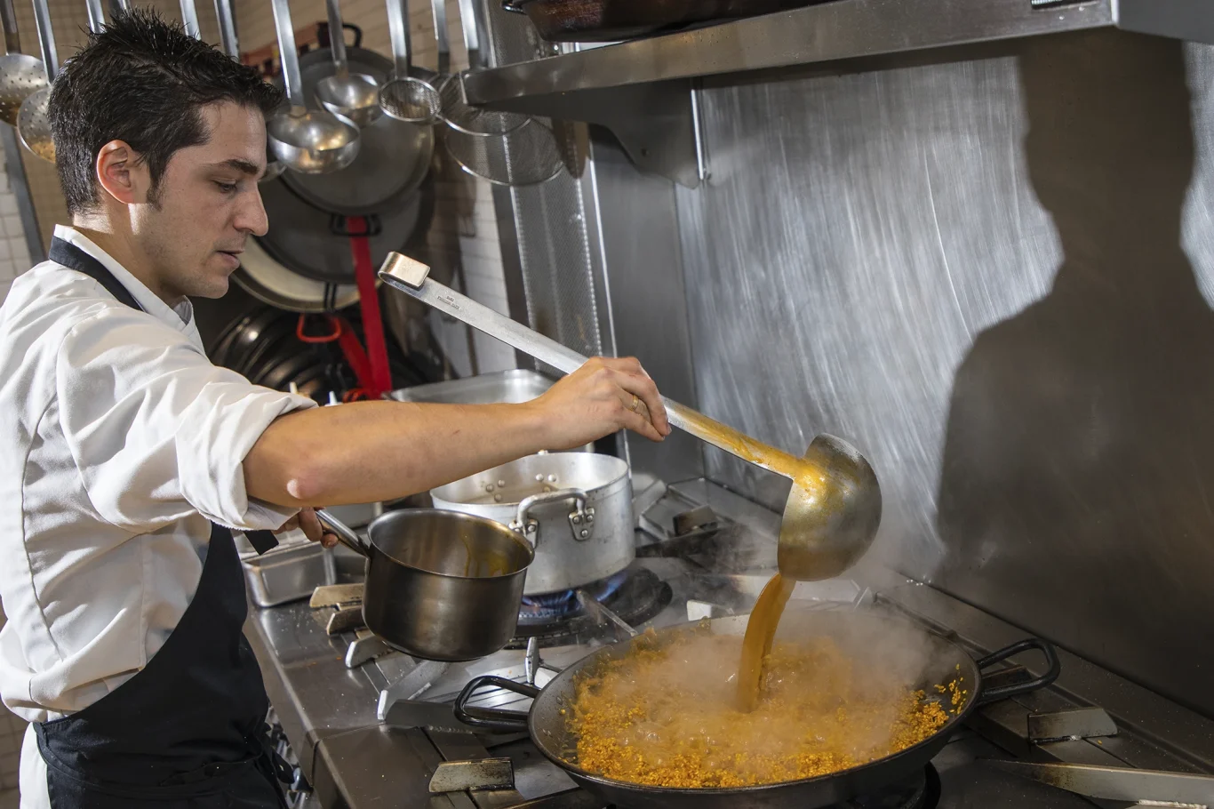 Koch verwendet Schöpflöffel mit langem Griff zum herstellen einer Paella