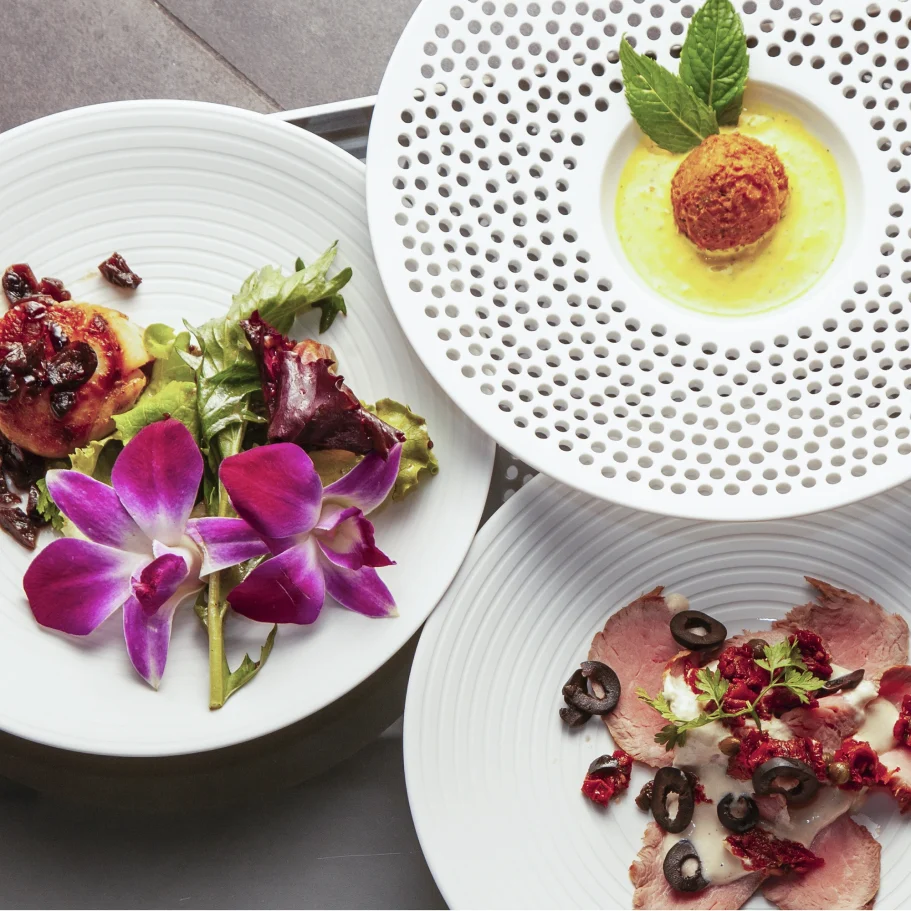 Drei Teller mit Vorspeise, Hauptspeise, Nachtisch und dekorativen Blumen.
