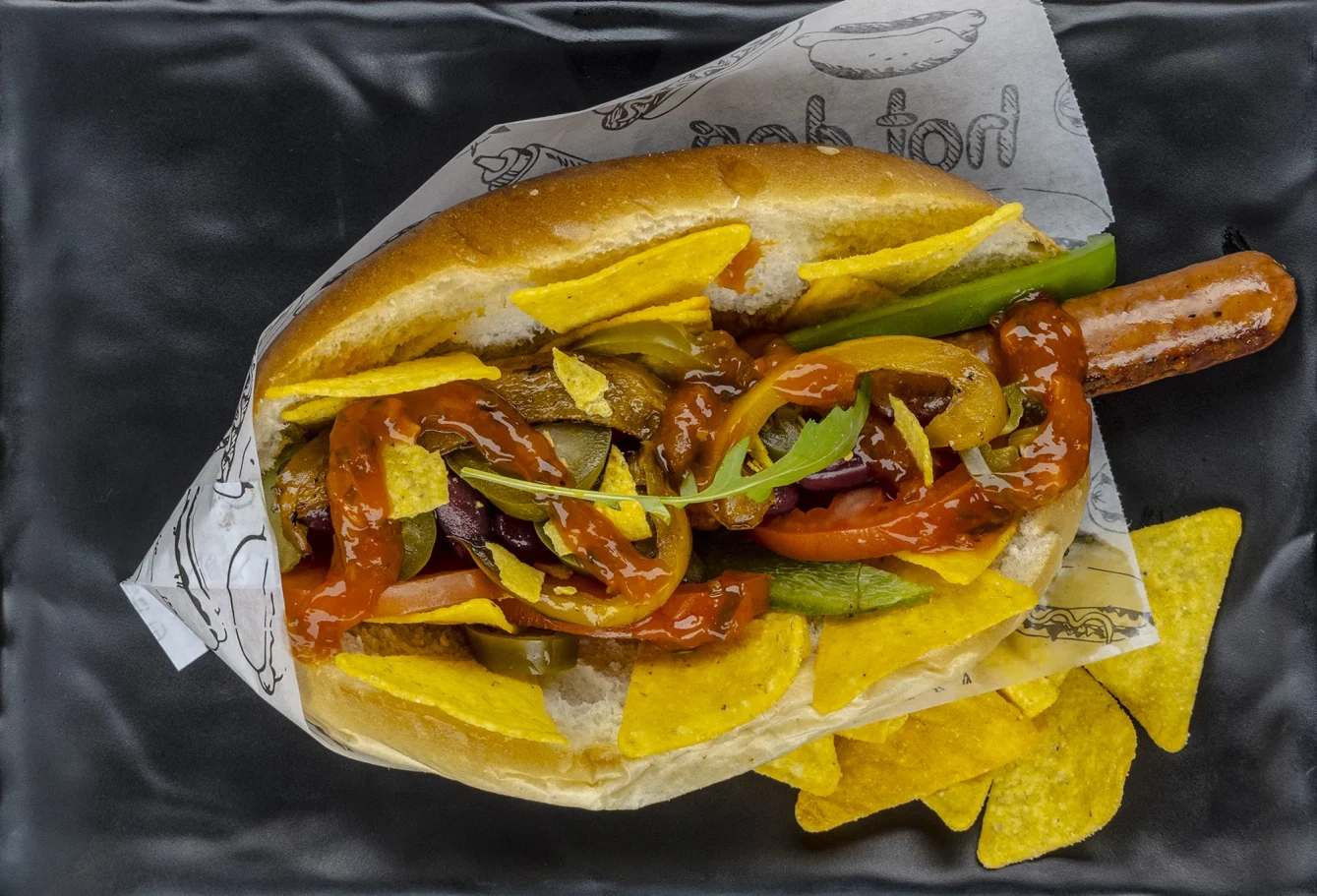Hot Dog mit Paprika, Zwiebeln, Senf und Tortilla-Chips.