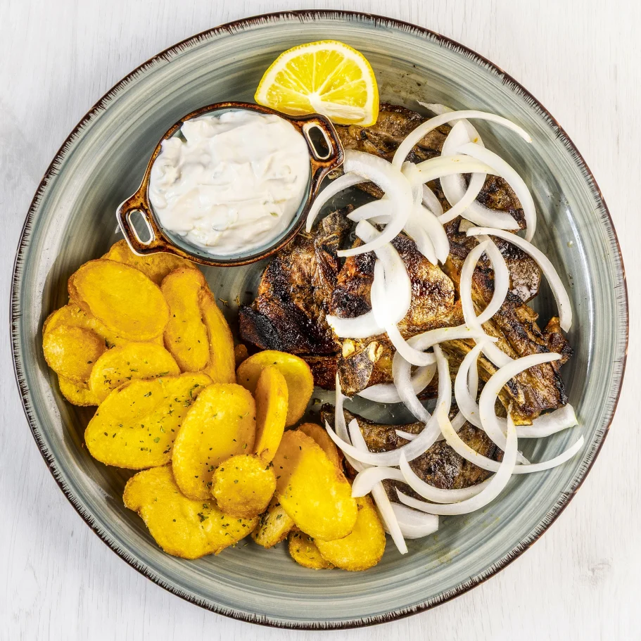 gegrillte Lammkoteletts mit Zwiebeln, Kartoffelchips und einer Schale Sauce, garniert mit Zitrone.